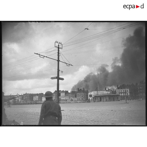 Plan général d'une partie du port de Dunkerque, une lourde fumée se dégage de la ville en arrière-plan.