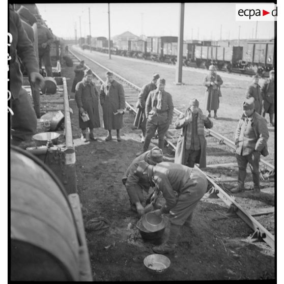 Des soldats perçoivent leur ration pour le repas le long d'une voie ferrée en gare de Trappes.