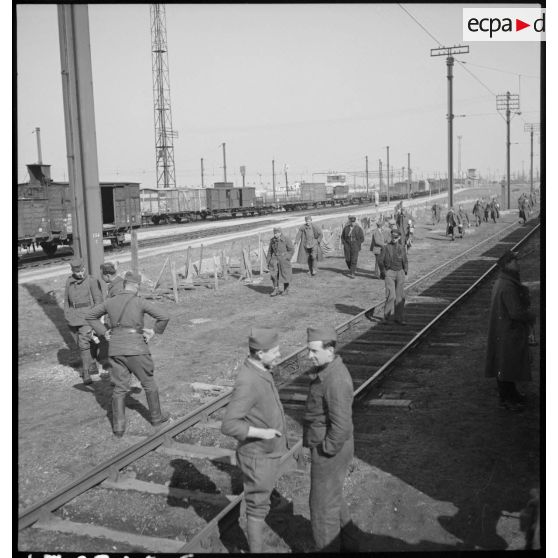 En gare de Trappes plan général d'une voie ferrée près de laquelle des soldats debout attendent.