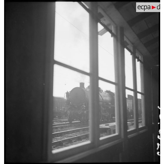 En gare de Trappes une locomotive est photographiée au travers de la fenêtre d'un baraquement.