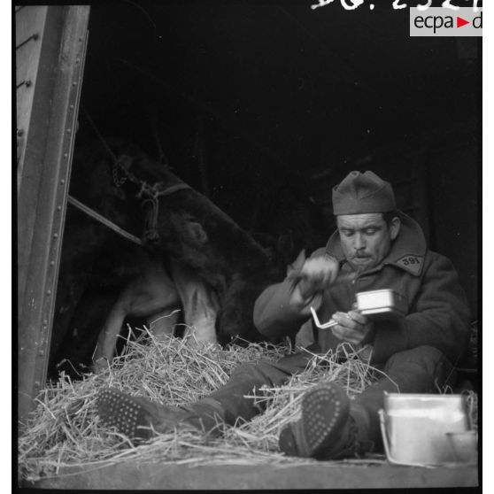 Un soldat mange assis à la porte d'un wagon de marchandises.