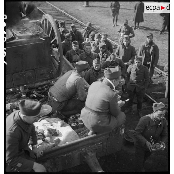 Des soldats perçoivent leur ration pour le repas le long d'une voie ferrée en gare de Trappes.