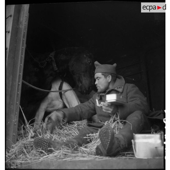 Un soldat mange assis à la porte d'un wagon de marchandises.