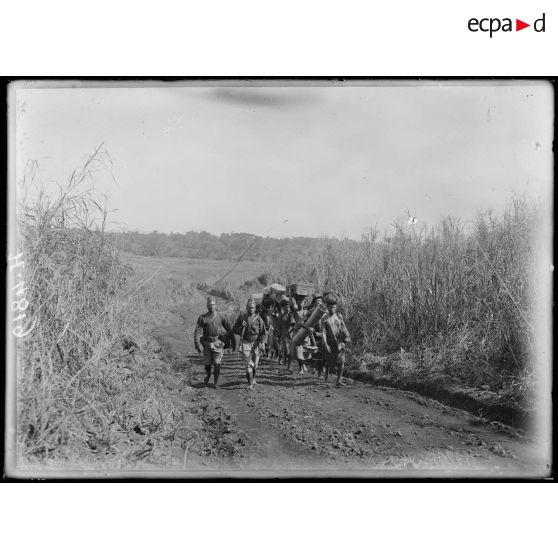 Route de Baré à Mbureku. Porteurs. Au fond, derniers palmiers à huile sur les contreforts du Manengouba. [légende d'origine]