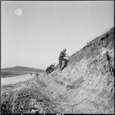 Des légionnaires montent un talus bordant une route lors d'une manœuvre en Oranie.