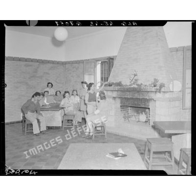 Photographie de groupe des personnels féminins réunis dans une salle commune, autour d'une table, près d'une cheminée.