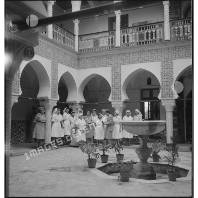 Photographie de groupe de personnel féminin infirmier et médical, dans une cour intérieure entourée d'arcades, ornée d'une fontaine.
