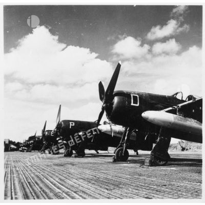Des avions de chasse Bearcat du GC 1/8 Saintonge chargés de bombes au napalm alignés sur le sol d'une base aérienne.