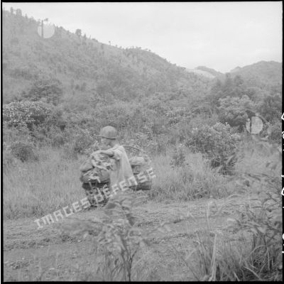 Soldat du Viêt-minh portant paquetages et munitions de mortier sur une palanche, photographié à son insu.