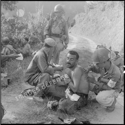 Le sergent-chef Filc se fait soigner par un infirmier indochinois sur le terrain.