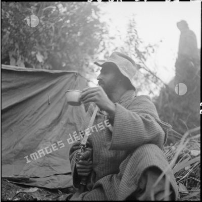 Un goumier du 2e tabor prend son café, armé d'un pistolet-mitrailleur MAT 49, au campement établi dans les montagnes au cours d'une opération au nord de Laï Chau.