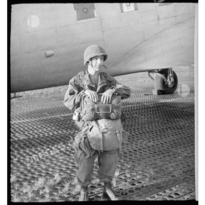 Un parachutiste du 2/1 RCP (2e bataillon du 1er régiment de chasseurs parachutistes) equipé pour leur saut, pose devant un avion Douglas C-47 sur le terrain d'aviation de Tong.