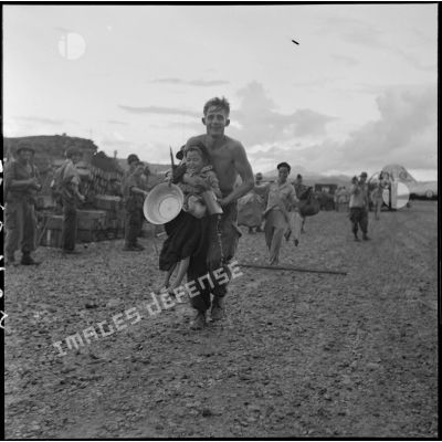 Le soldat Michel du 1er bataillon Thaï porte dans ses bras une petite fille Thaï sous le regard amusé d'autres fantassins, au cours de l'évacuation du camp retranché de Na San.