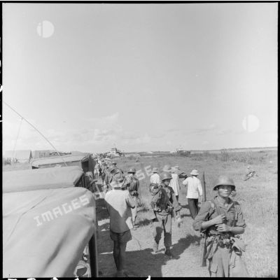 Une colonne de soldats venant de débarquer d'un LCT croise des brancardiers transportant les morts et les blessés d'un récent engagement, au cours de l'opération Claude.