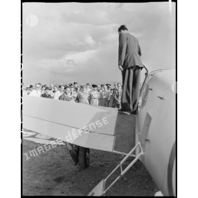 Une personnalité civile se tient debout sur l'aile d'un avion triplace de tourisme, sous le regard de personnalités civiles et militaires.