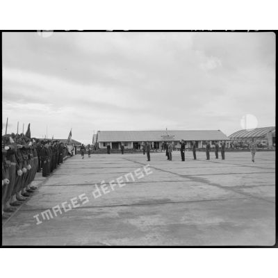Plan d'ensemble d'une cérémonie militaire, sur un aérodrome, à laquelle assiste le général Philippe Leclerc, accompagné d'autorités militaires.