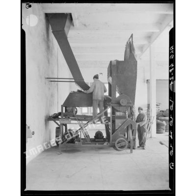 Deux hommes travaillent sur une machine, certainement un moulin à farine, à Maison-Carrée.