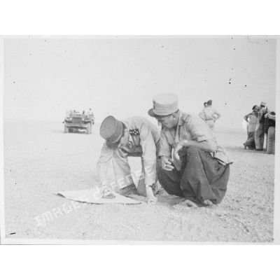 Le général Philippe Leclerc consulte une carte, accompagné d'une personnalité militaire, dans le désert du Fezzan.