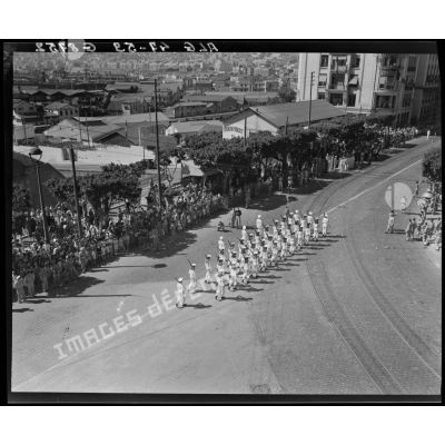 Plan en plongée du défilé d'une unité de la Marine nationale, sous le regard d'autorités militaires, civiles et de la population civile, à Alger.