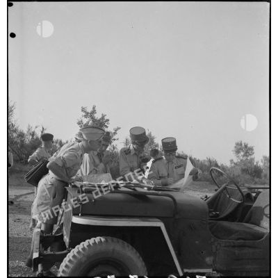Le général Philippe Leclerc consulte une carte sur le capot d'un véhicule militaire, assisté d'autorités militaires.