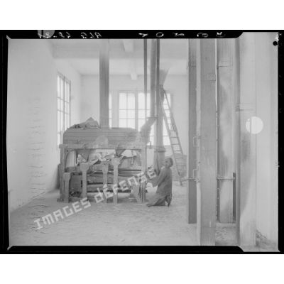 Un homme travaille sur une machine, peut-être un moulin à farine, à Maison-Carrée.
