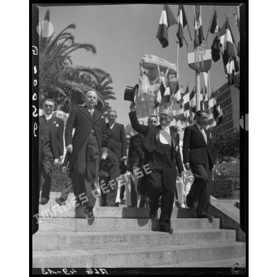 Le président de la République Vincent Auriol descend les marches, devant le monument aux morts d'Alger, en saluant la foule, accompagné d'autorités civiles.