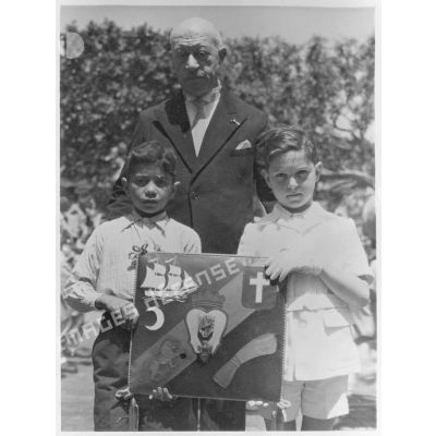 Portrait de groupe rassemblant une autorité civile et deux petits garçons qui tiennent le coussin aux armes d'Alger, avec la croix de guerre.
