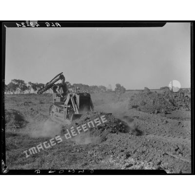 Un militaire nivèle un terrain avec un bulldozer équipé d'une tarière.