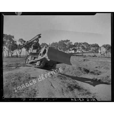 Un militaire test un bulldozer équipé d'une tarière sur un terrain bosselé.
