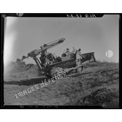 Un militaire test un bulldozer équipé d'une tarière sur un terrain en pente.