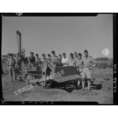 Photographie de groupe rassemblant des autorités militaires autour d'un bulldozer équipé d'une tarière.