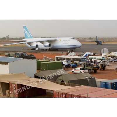 Derrière une zone de regroupement logistique, un avion-cargo de transport Antonov 124-100 ukrainien stationne sur une piste de l'aéroport de Bamako, pendant le roulage d'un Transall C-160 français.