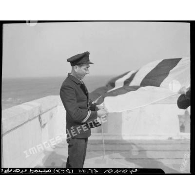 Le chef de poste vérifie l'amarrage des pavillons, sur la terrasse d'un sémaphore, face à la mer.