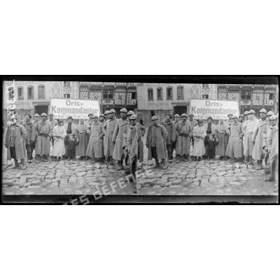 Roye, Somme. Groupe de poilus et de femmes devant l'écriteau de la Kommandantur. [légende d'origine]