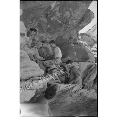 Des soldats se restaurent à l'abri d'un rocher. [légende d'origine]