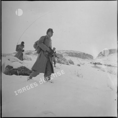 Des soldats du 8e RIM progressent sur un terrain enneigé. Sur la gauche, le radio semble en communication. [légende d'origine]