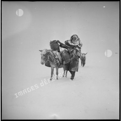Un homme effectue une corvée d'eau sous la neige. Des mulets transportent les tonneaux. [légende d'origine]
