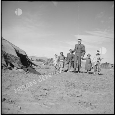 [Portrait d'un homme et de quelques-uns de ses jeunes élèves dans le camp d'habitation des khaïmas.]