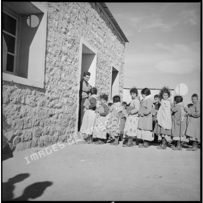 Les enfants attendent en rang devant l'entrée de l'école. [légende d'origine]