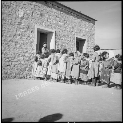 Les enfants attendent en rang devant l'entrée de l'école. [légende d'origine]