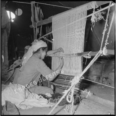 A l'intérieur d'une khaïma, une jeune femme travaille sur son métier à tisser. [légende d'origine]