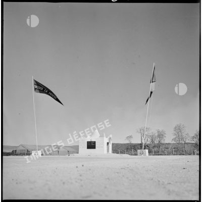 Vue d'ensemble du marabout du commando Georges. Le monument est encadré par deux drapeaux, sur la droite, le drapeau français et sur la gauche le drapeau du commando sur lequel est inscrite la devise du commando : " Chasser la misère ". [légende d'origine]