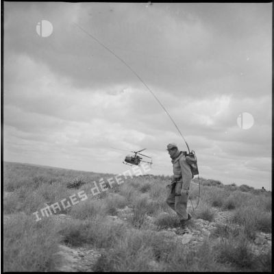 Vue d'un radio sur le terrain à l'occasion d'une opération menée par la 2e compagnie du 8e RIM. En arrière-plan, dans les airs, un hélicoptère de type Alouette passe en rase-motte. [légende d'origine]