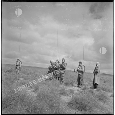 Sur le terrain, trois radios accompagnent un officier de la 2e compagnie du 8e RIM qui observe une carte des environs, au cours d'une opération militaire. [légende d'origine]