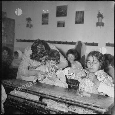 Apprentissage professionnel. Dans une salle de classe, une enseignante s'occupe de l'apprentissage du tricot auprès de ses jeunes élèves. [légende d'origine]