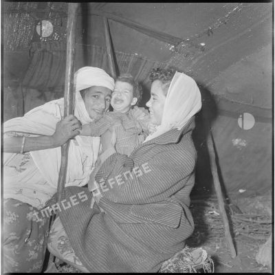 Portrait d'une membre d'une EMSI, d'une femme et d'une jeune enfant à l'intérieur d'une khaïma au cours d'une séance d'auscultation. [légende d'origine]