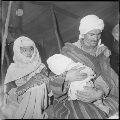 Portrait d'un homme, d'une femme et de leur bébé à l'intérieur d'une khaïma. Ils attendent leur tour pour faire ausculter leur enfant. [légende d'origine]