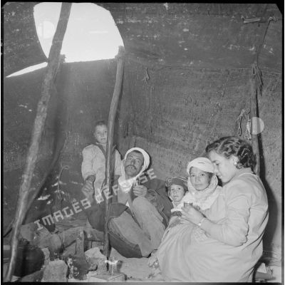 Portrait d'une famille à l'intérieur d'une khaïma. Sur la droite, une infirmière (EMSI) venue pour une séance d'auscultation boit le thé. [légende d'origine]