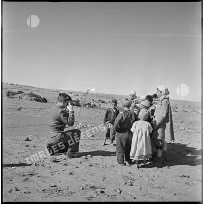 Un soldat photographie un groupe d'enfants du village. En arrière-plan, on distingue plusieurs khaïmas. [légende d'origine]