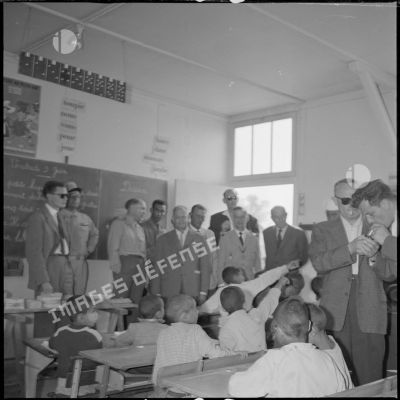 Les autorités civiles et militaires visitent une salle de classe. On peut lire la date du vendredi 3 juin au tableau. [légende d'origine]